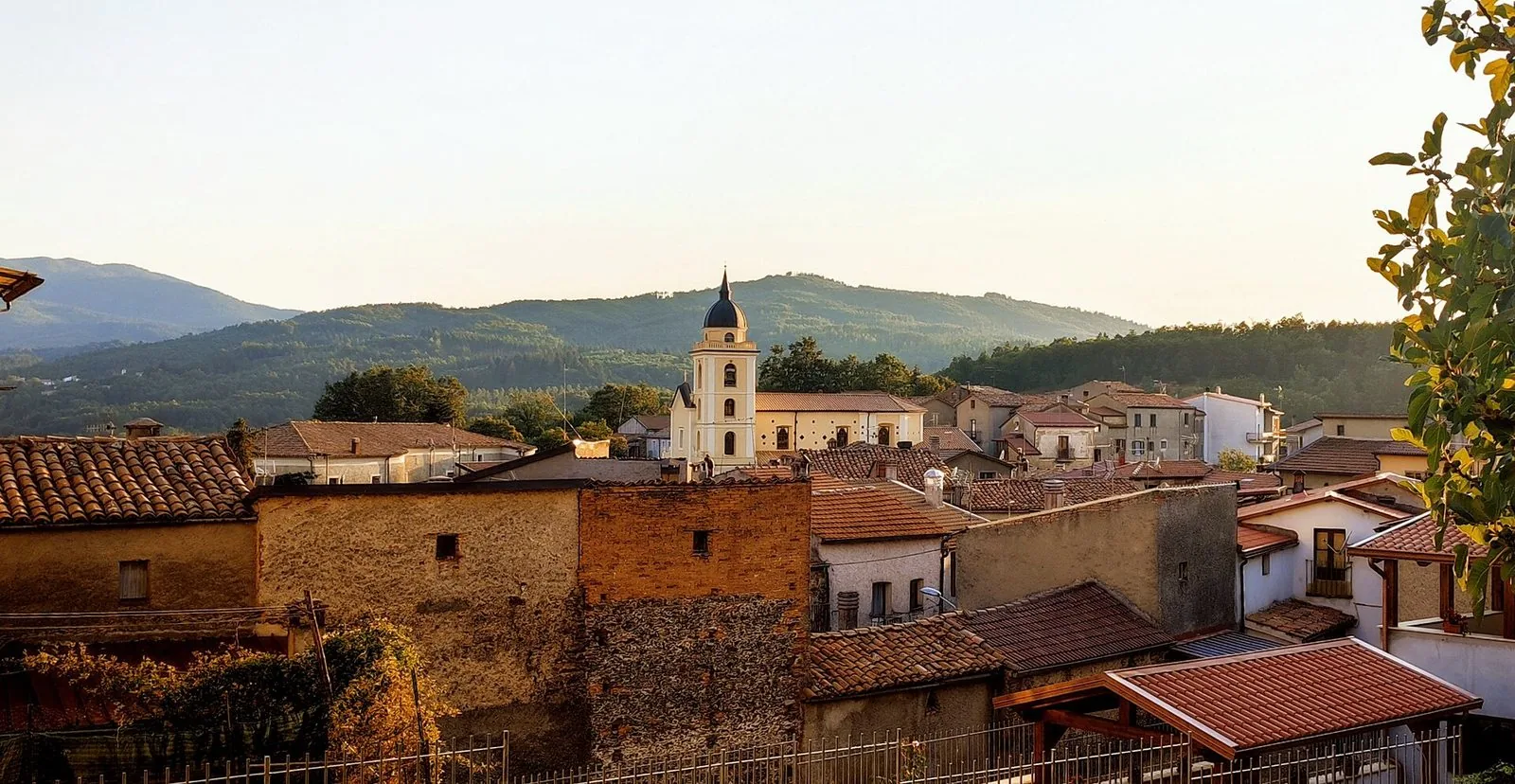 I tetti del centro storico di Soveria Mannelli con il campanile della chiesa illuminato dal sole del tramonto e le colline boscose sullo sfondo