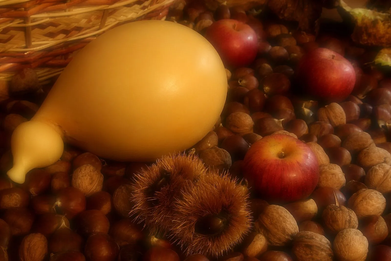Un caciocavallo intero adagiato su un letto di castagne, noci e mele rosse, accanto a un cesto di vimini
