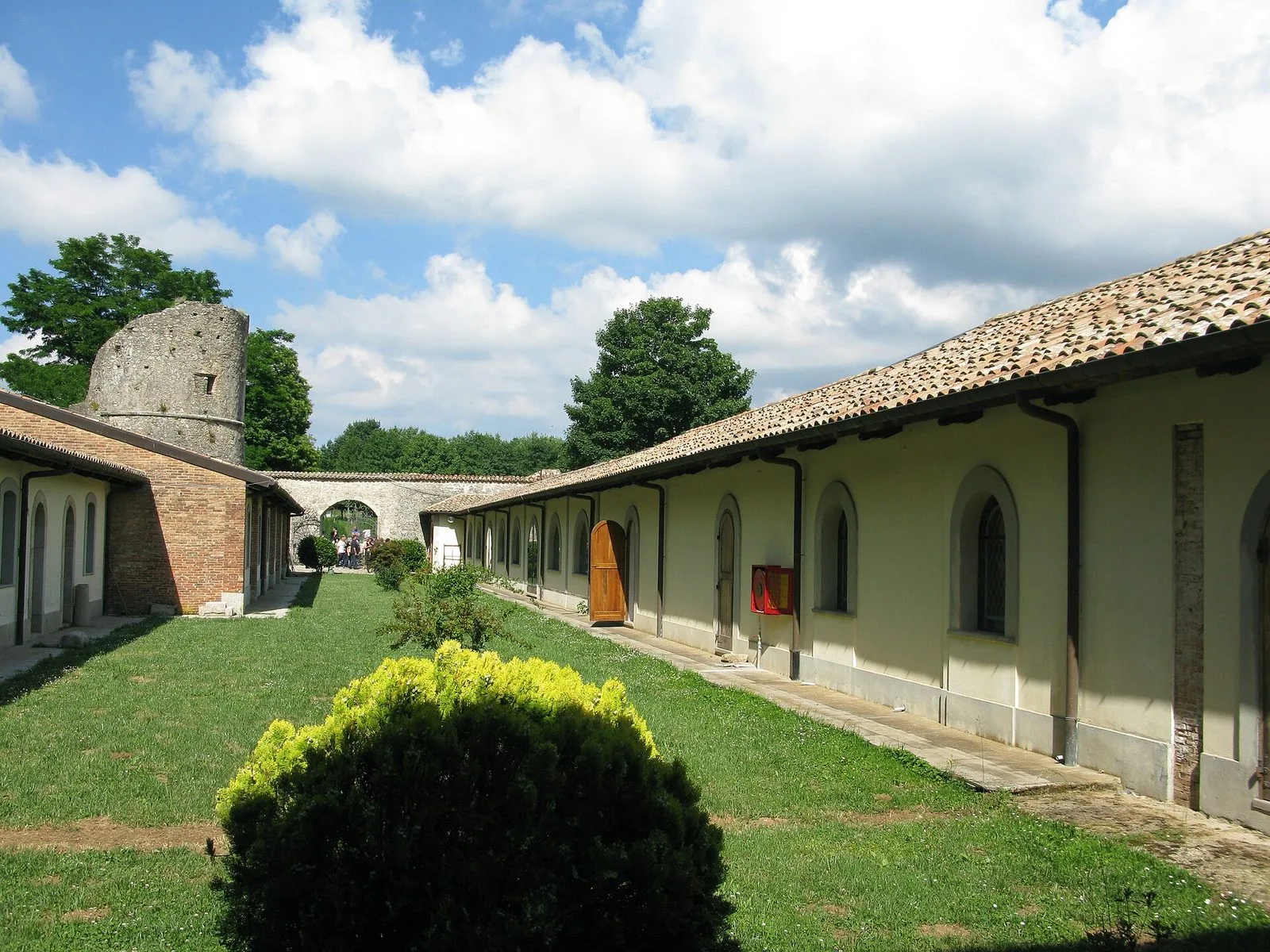 Il cortile erboso del Museo della Certosa di Serra San Bruno, con le celle dal tetto in coppi, una torre in pietra e alberi sullo sfondo
